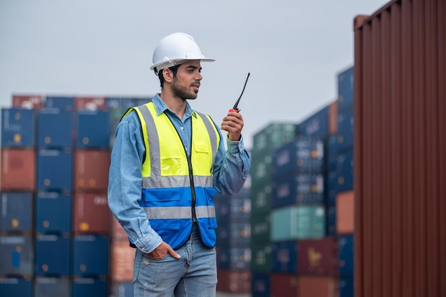 Logistiek manager praten op de walkietalkie in containermagazijn voor controle laden van containers in containerwerfterminal verzending Arbeiderscontainer pratende radio om de export van goederen te beheren