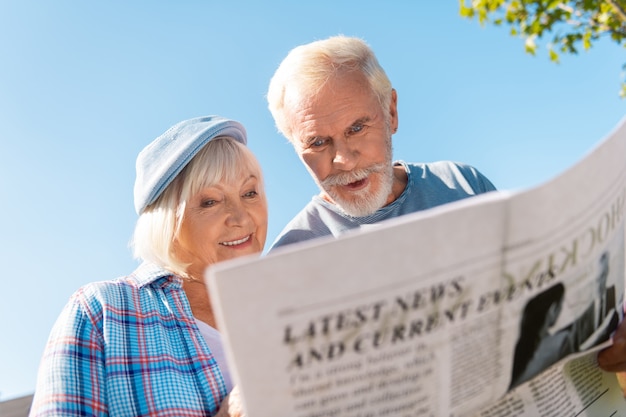 Lokaal nieuws. Bejaarde echtpaar voelt zich echt betrokken en opgewonden tijdens het lezen van lokaal ochtendnieuws buiten het huis