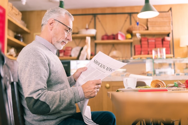 Lokale krant. Rijpe grijsharige man die erg nieuwsgierig is en betrokken is bij het lezen van de lokale krant