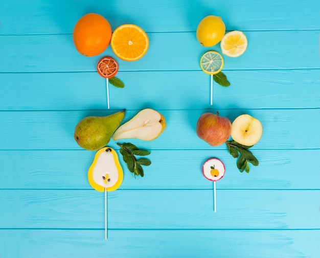 Lollipops as a pear, orange, lemon and apple on wooden turquoise desk near delicious sliced fruits with a sprig of mint