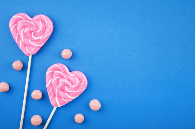 青い背景のロリポップとキャンディードラジェのお菓子と砂糖棒の上のおいしいピンクのハート