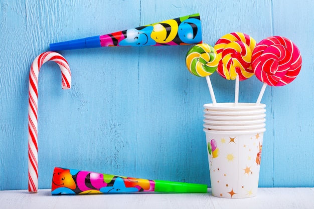 Lollipops in cups with candy canes and whistles on blue wooden wall