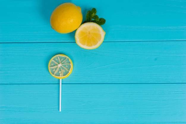 Lolly als een citroen op een houten turquoise bord in de buurt van heerlijke gesneden citroen en een takje munt