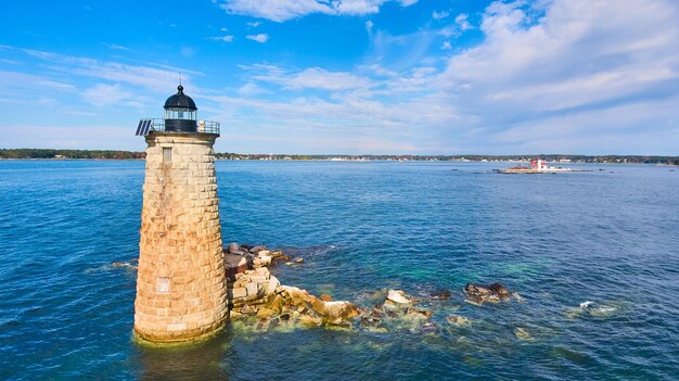 Lone stone tower lighthouse on broken rocks in maine ocean