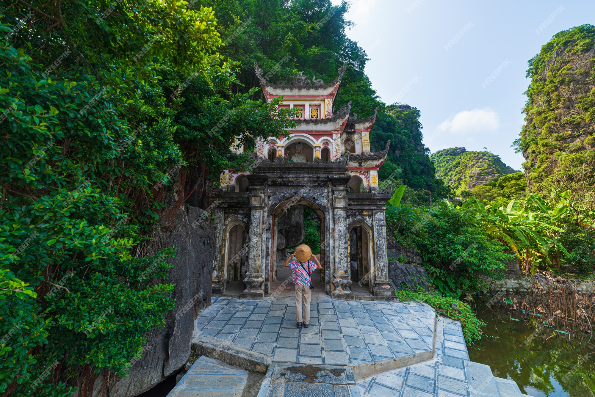 Premium Photo  Lone tourist with traditional vietnamese hat at bich dong  pagoda entrance gate, ninh binh vietnam, buddhist temple set amid jungle  and karst mountain range. traveling alone, keep social distancing.