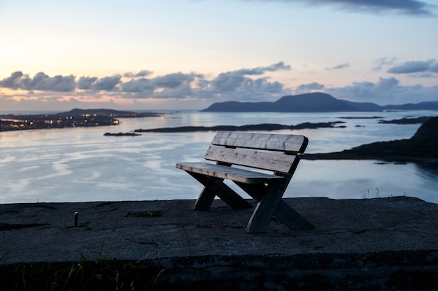 A lone wooden bench stands on top of a mountain. Sunset evening time