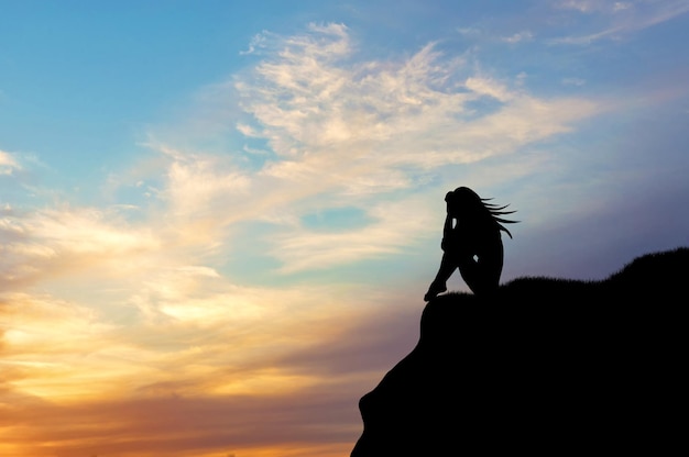 Loneliness concept. Silhouette of a woman alone on a hill at sunset