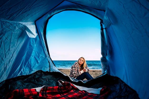 Lonely beautiful blonde girl out of the tent on the beach for alternative freedom camping open air. vacation on the beach near the ocean waves for surfer blonde girl lifestyle californian way