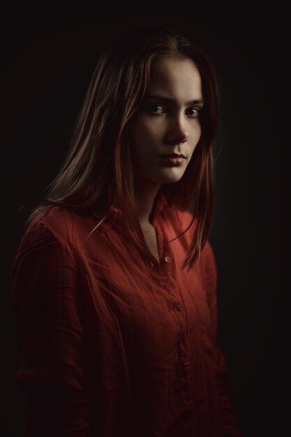 Lonely beautiful woman in coral shirt attentively looking at a camera on dark background