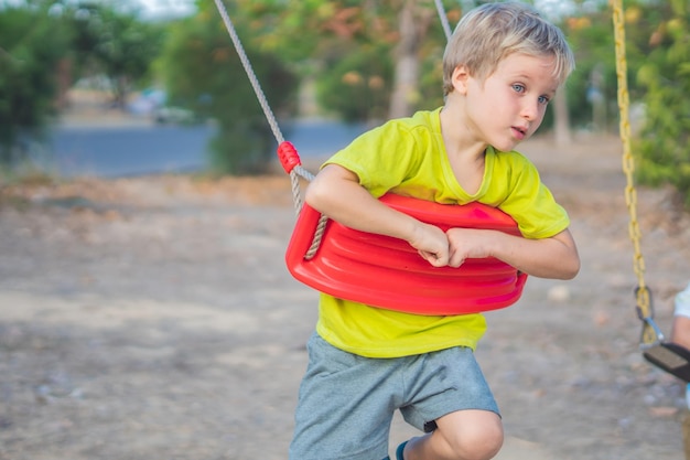 友達や両親を待っているブランコに座っている孤独な少年夏の子供時代のレジャー友情の人々は何か新しい概念に興味を持っています