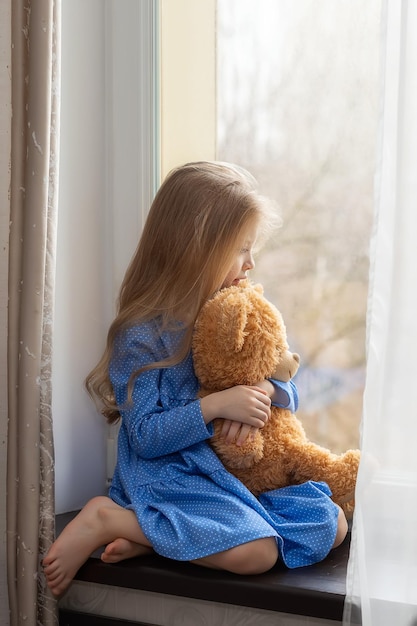 A lonely child sits on the windowsill and looks out the window Autism concept closeup portrait