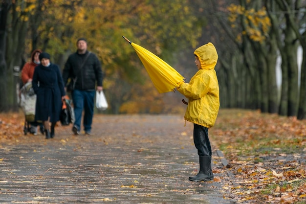 Lonely child in yellow raincoat with umbrella in an autumn park against the background of people