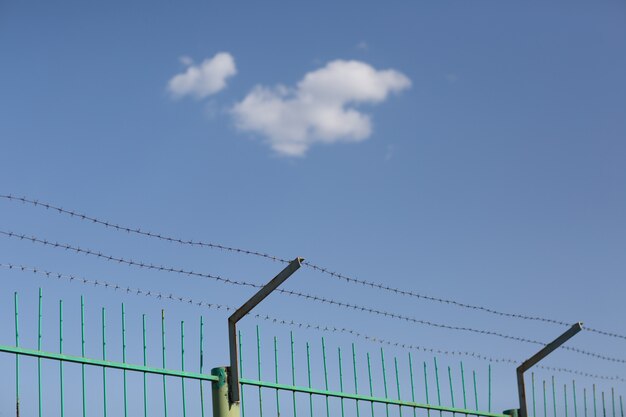 Lonely cloud in blue sky behind barbed wire