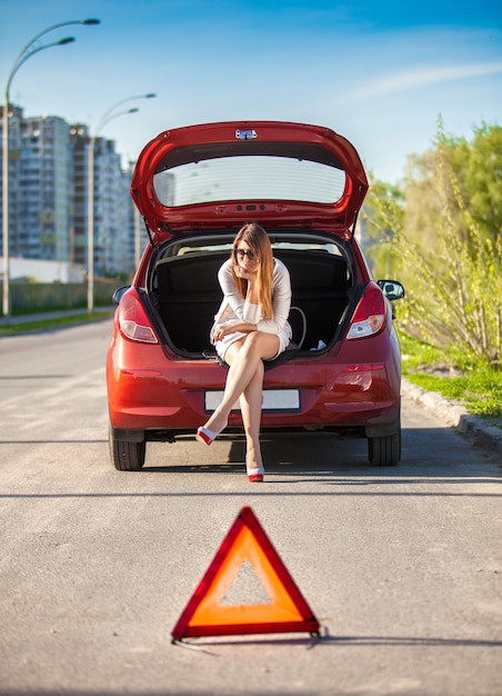 Lonely depressed woman sitting on trunk of broken car