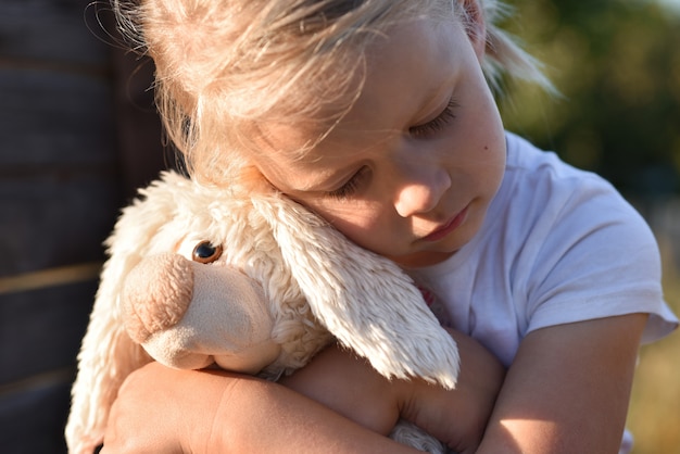 Photo lonely girl on the street is sad and holds a toy hare with hands