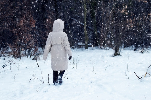 Una ragazza sola cammina nel parco in inverno durante una nevicata