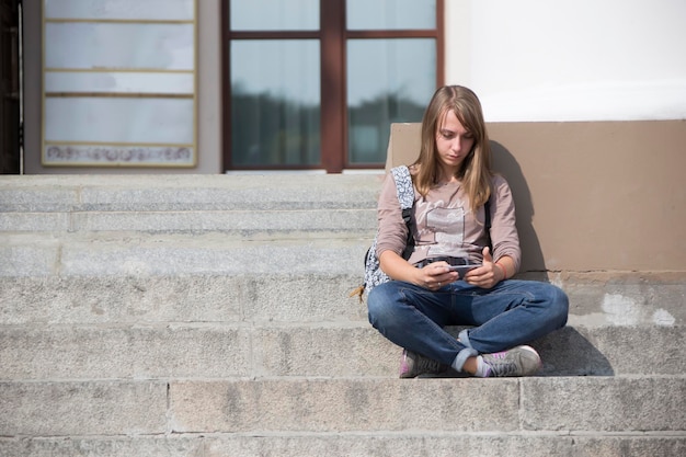 Una ragazza sola con un telefono si siede sui gradini