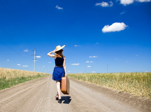 Lonely girl with suitcase at country road.