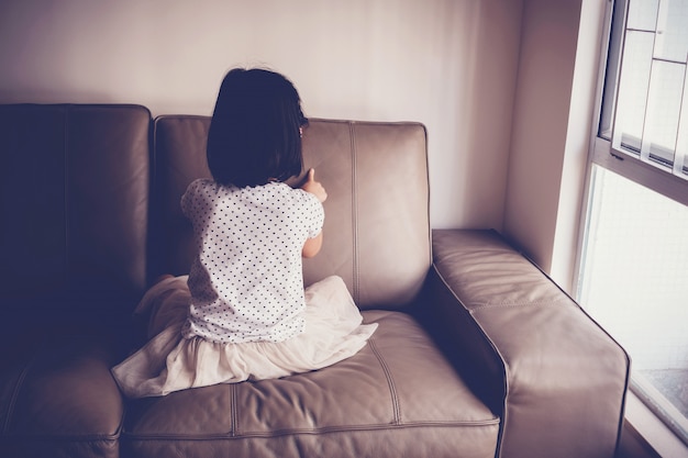 Lonely little girl playing by herself on sofa at home, austism and child mental health concept