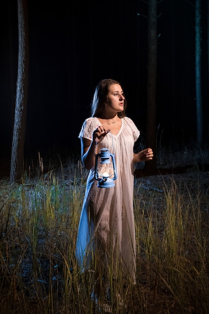 Lonely lost woman in forest at night walking with candle lantern