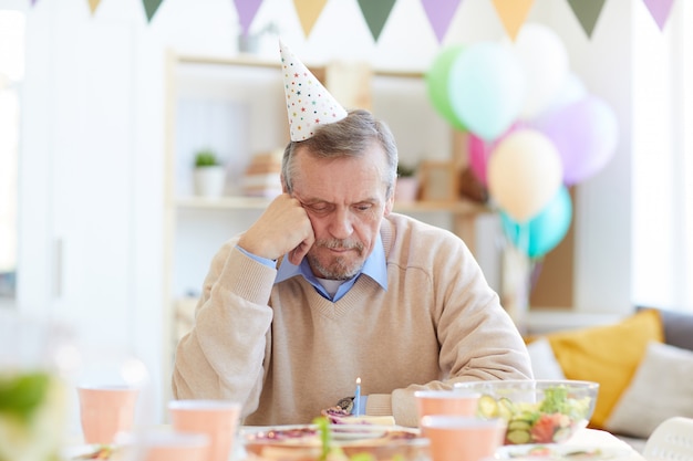 Lonely man looking at birthday cake with candle