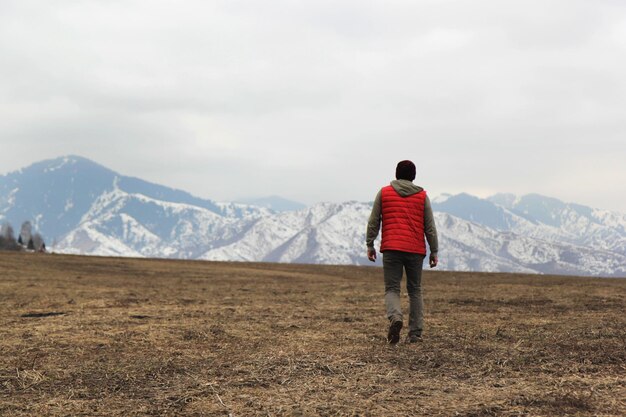 Photo lonely man in red waistcoat walking toward mountains background