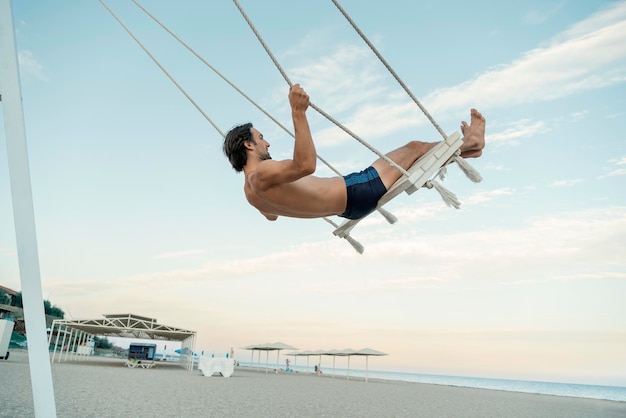 Lonely man silhouette swinging at sunset on the beach Young guy has fun by the sea