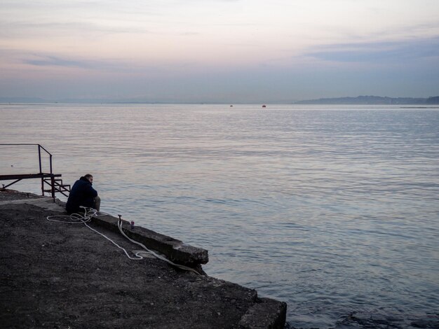 lonely man sits on the pier in the evening A man is sitting in the port area Loneliness concept Port city in winter At dusk