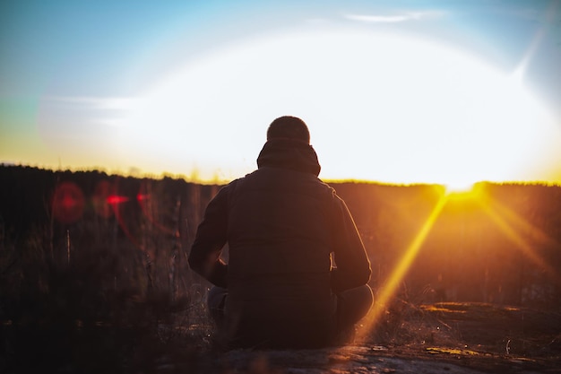 孤独な男が座って、劇的な夕日と孤独を見て