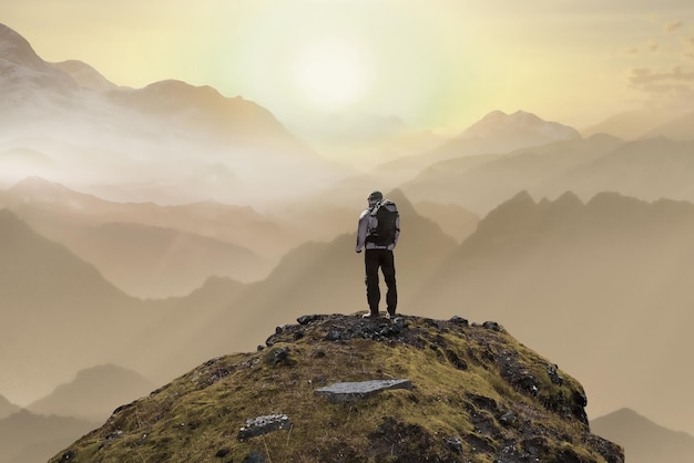 A lonely man on the top of the mountain stands with his back and looks at the sunset