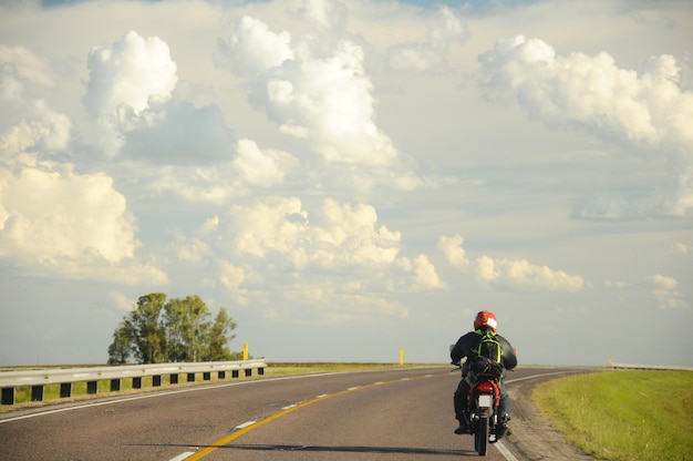 孤独なモーターサイクリストが右に曲がる道を走り、背景に雲がいっぱいの空