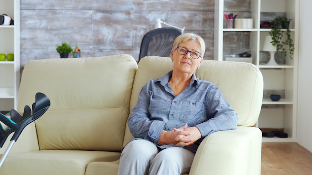 lonely old woman sitting on couch in a nurshing home keeping hands together