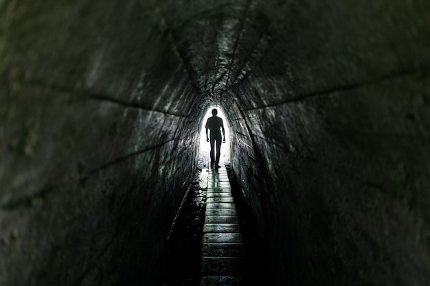 暗いトンネルの中の孤独な通行人。トンネルの終わりに光が当たる。
