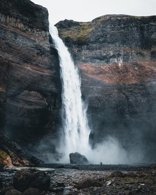 Одинокий человек наслаждается прекрасным видом на водопад, окруженный скалистыми скалами в Исландии