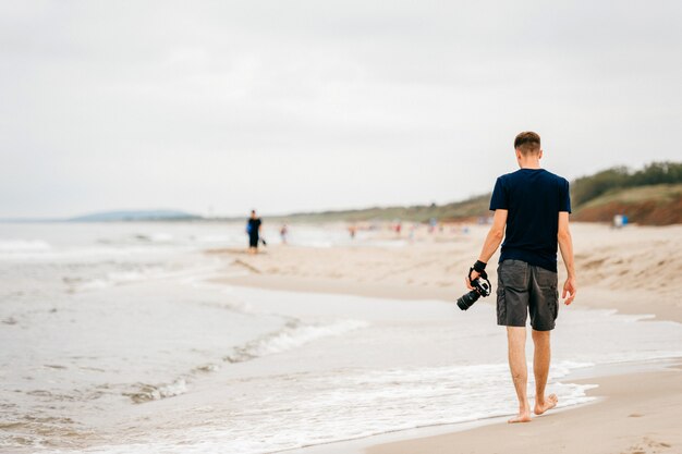 Lonely photographer with a camera in his hand walking along sea.