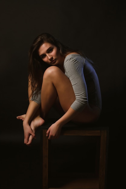 Lonely sad brunette woman sitting on a chair in the dark room