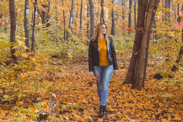 孤独な悲しい女性が秋に黄色の葉を蹴っています。悲しい気分と季節性情動障害の概念。