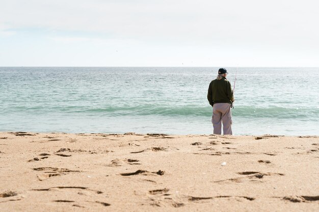 Lonely senior man fishing on the beach elder person enjoying\
retirement by the sea concept