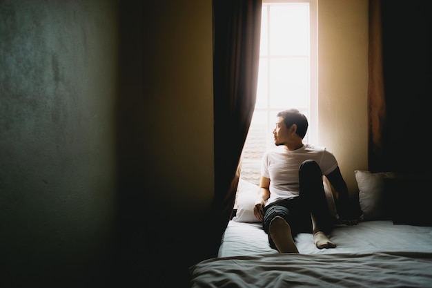 Lonely single man sit and rest alone in dark bedroom with light from curtain