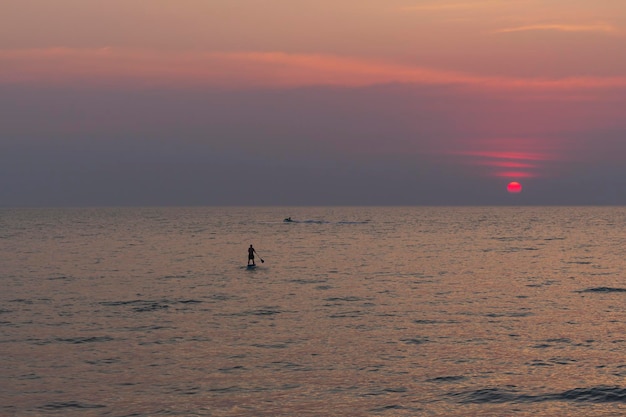 写真 孤独な sup ボードマン サーファーの帆が夕日の海の冒険に向かって海水の上を移動します。