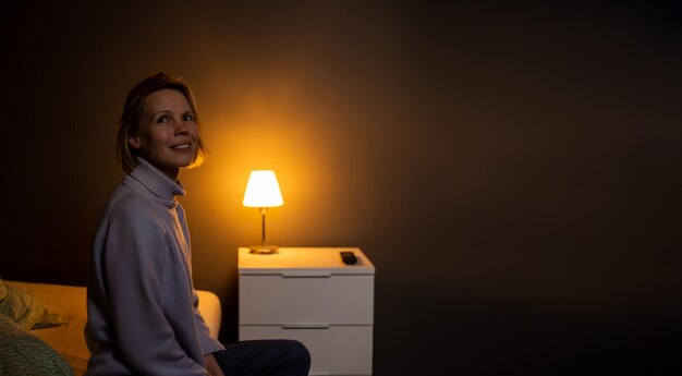 Lonely woman in a dark room The lamp next to the bed is on Place for text