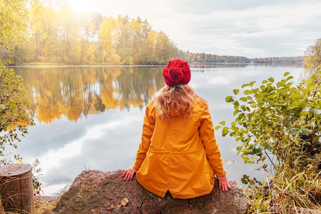 Lonely woman is sitting on the shore of a forest lake