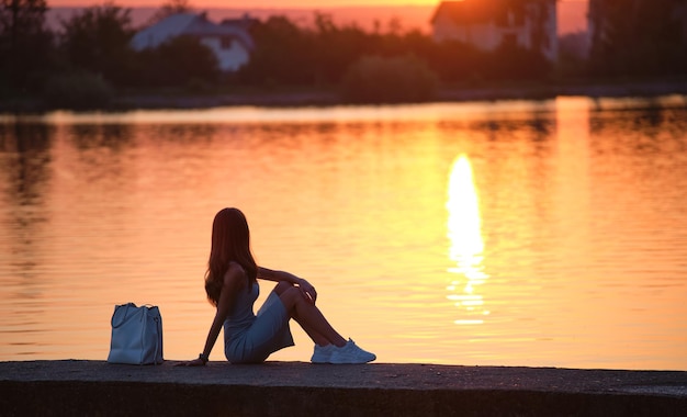 Donna sola seduta da sola sulla riva del lago in una calda serata solitudine e relax nel concetto di natura