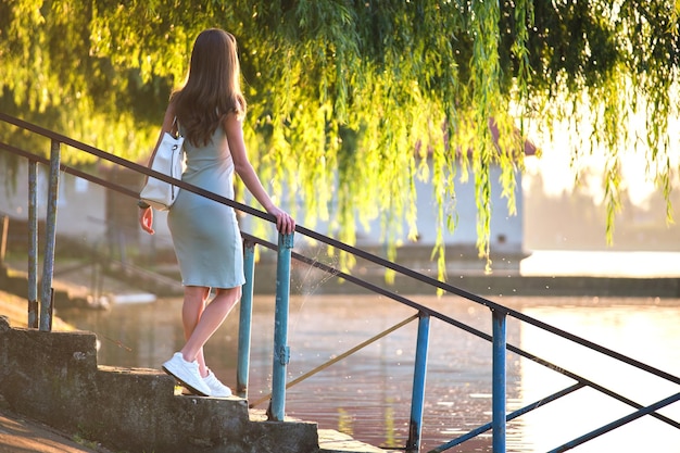 Lonely woman standing on lake side on warm evening. Solitude and relaxation concept.