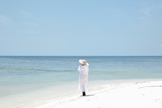 Lonely Woman tourist wearing summer hat enjoying sea view on white sandy beach in summer vacation