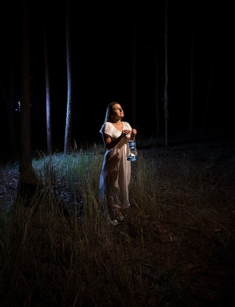 Lonely woman with gas lamp  standing in scary dark forest