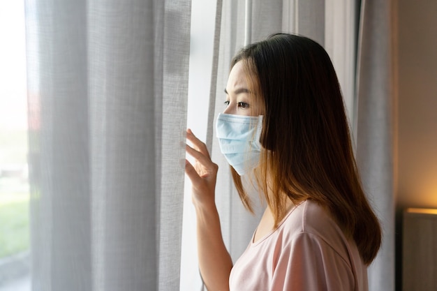 Lonely young Asian woman in sugical face mask stay isolation at home for self quarantine.