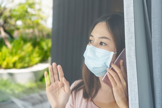 La giovane donna asiatica sola in maschera facciale zuccherina rimane isolata a casa per l'auto quarantena.