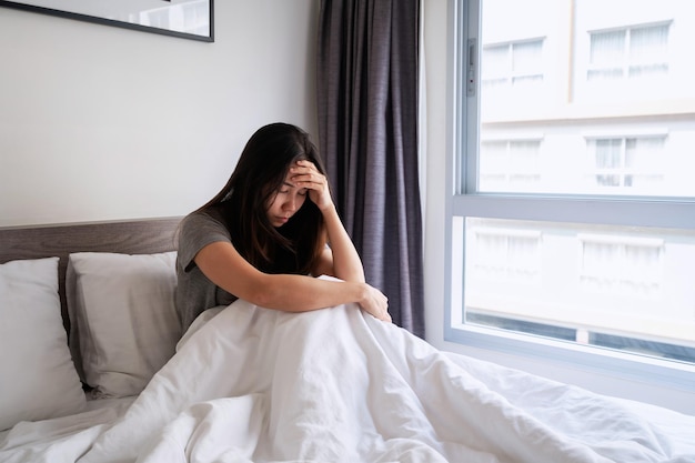 Giovane donna sola che si sente depressa e stressata seduta in camera da letto, emozione negativa e concetto di salute mentale