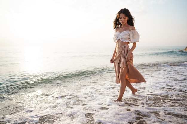 Lonely young woman walks on the seashore at sunset